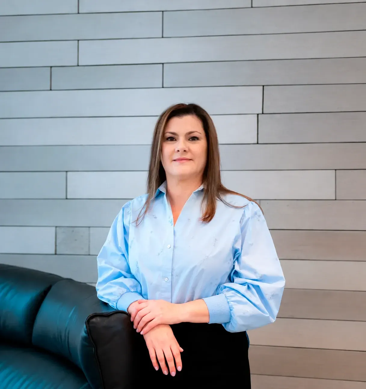 Ana Carolina Brocca, fundadora da Lauma Turismo, de camisa azul-clara, apoiada em um sofá de couro