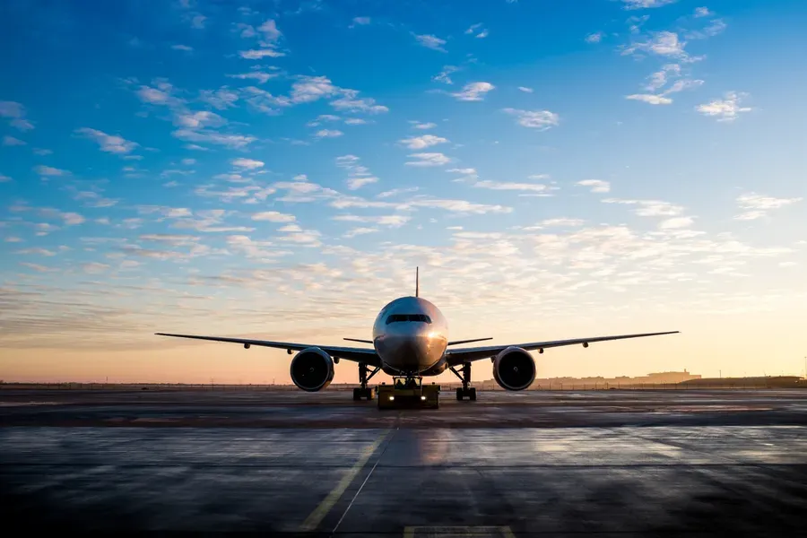 Avião na pista do aeroporto ao amanhecer, com céu azul e nuvens