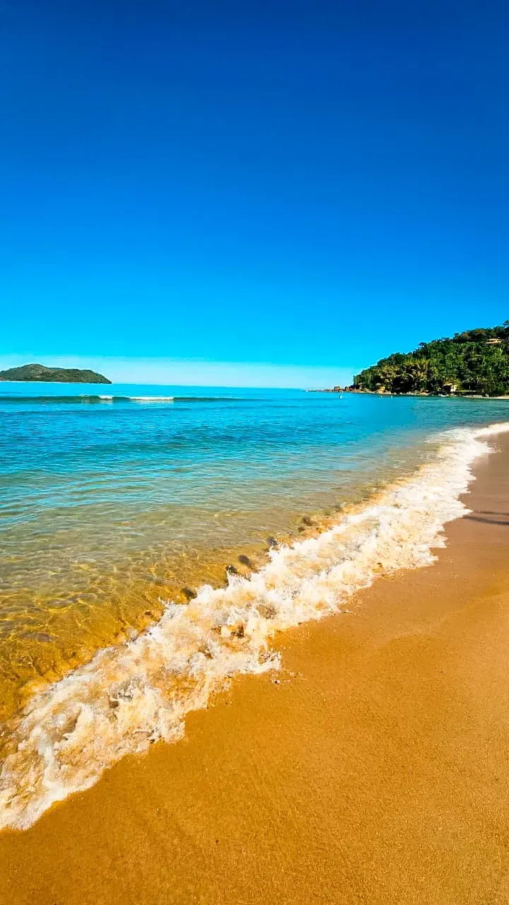 Praia de mar azul-turquesa e transparente com areia dourada e onda quebrando