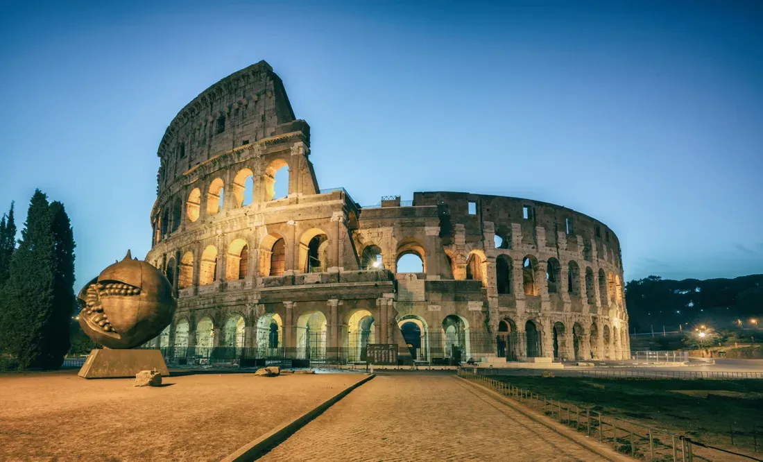 Coliseu de Roma iluminado ao entardecer, sob céu azul